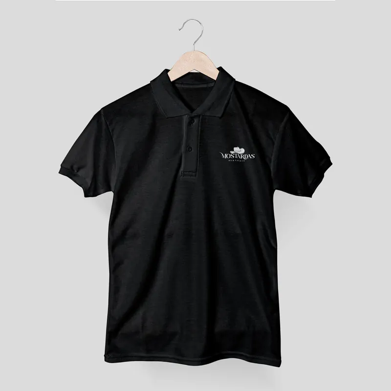 Polo preto num cabide, com o logótipo pequeno d'Os Mostardas no peito.